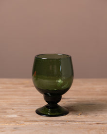 Green recycled glass goblet on a wooden surface with a brown background