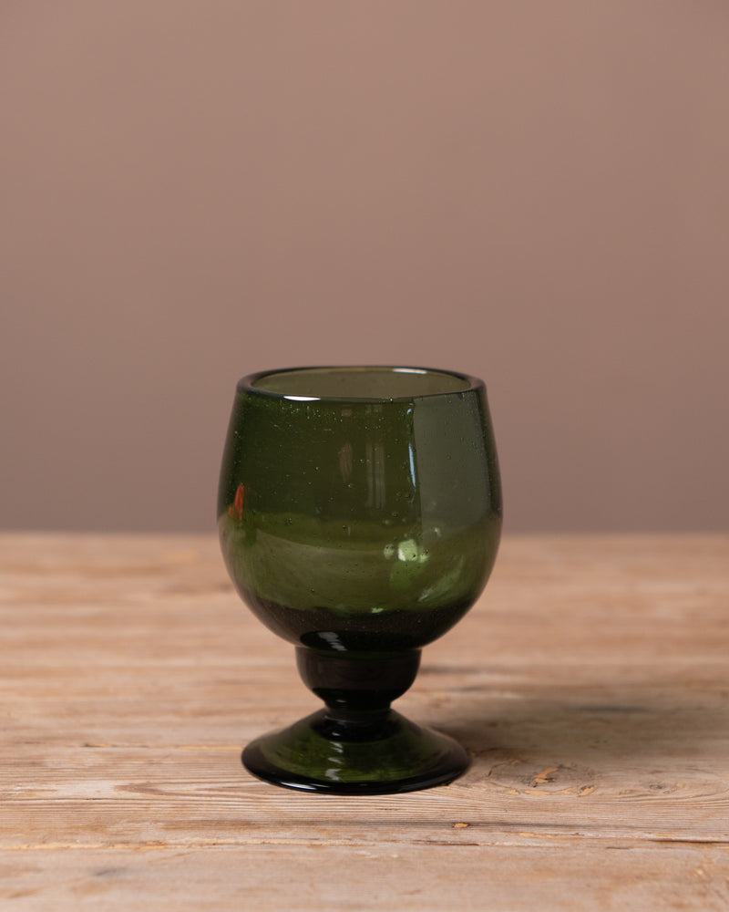 Green recycled glass goblet on a wooden surface with a brown background