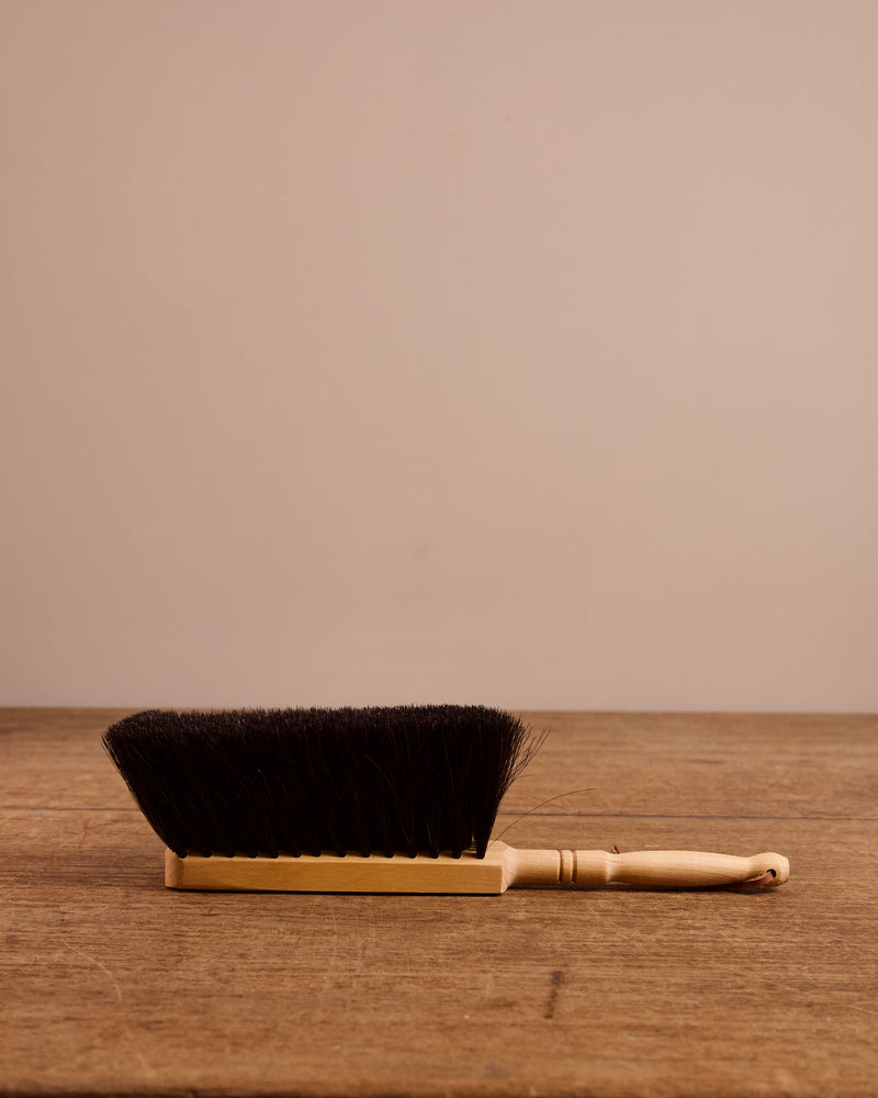 Handheld brush with black bristles on a wooden surface