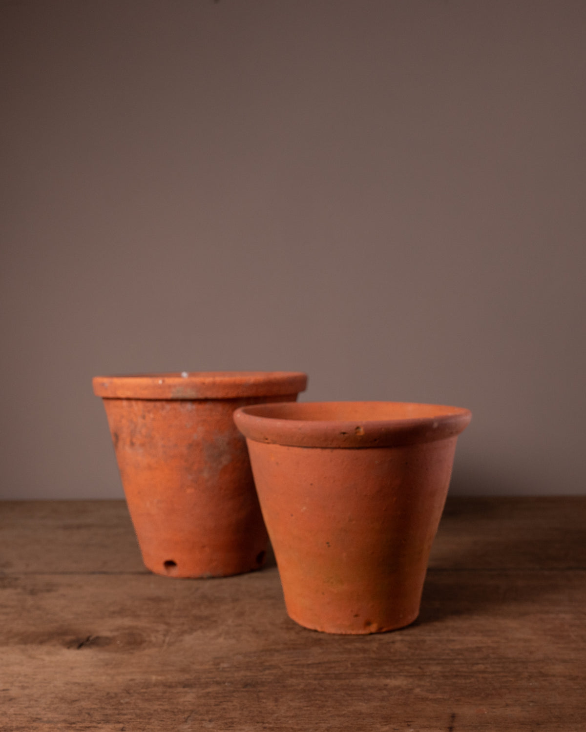 Two terracotta pots on a wooden surface with a brown background