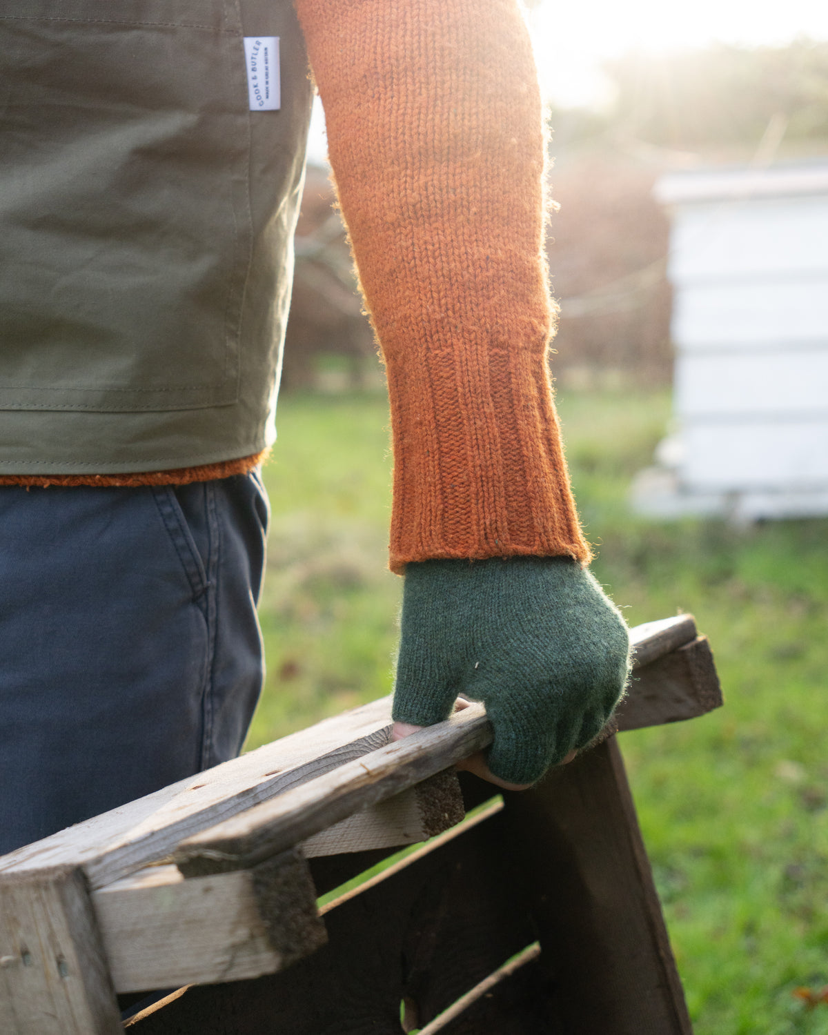 Person wearing green gloves holding a wooden crate outdoors