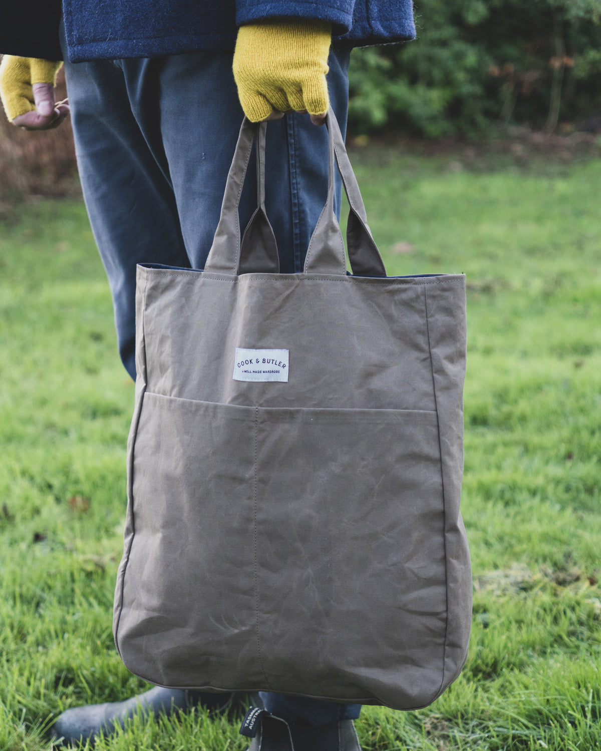 Person with yellow gloves holding a 'Cook and Butler' tote bag.
