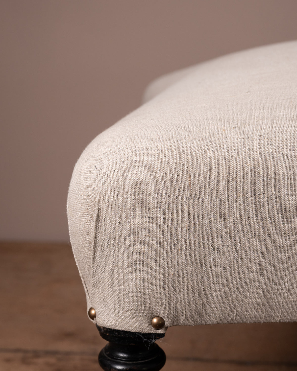 Close-up of a beige upholstered chair with a brown background