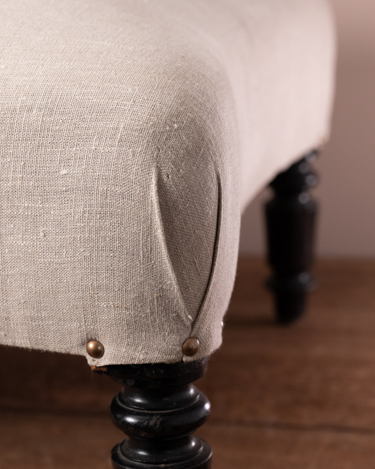 Close-up of a beige upholstered chair with dark wooden legs on a wooden floor.