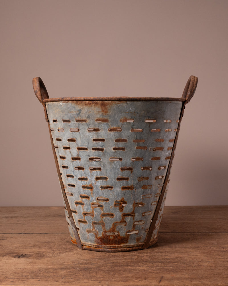 Rustic metal basket with handles on a wooden surface and brown background