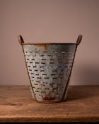 Rustic metal basket with handles on a wooden surface against a brown background
