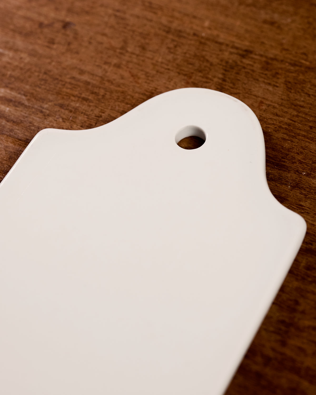 White ceramic cutting board with a hole on a wooden surface