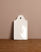 White ceramic cutting board with a hole on a wooden surface and beige wall background