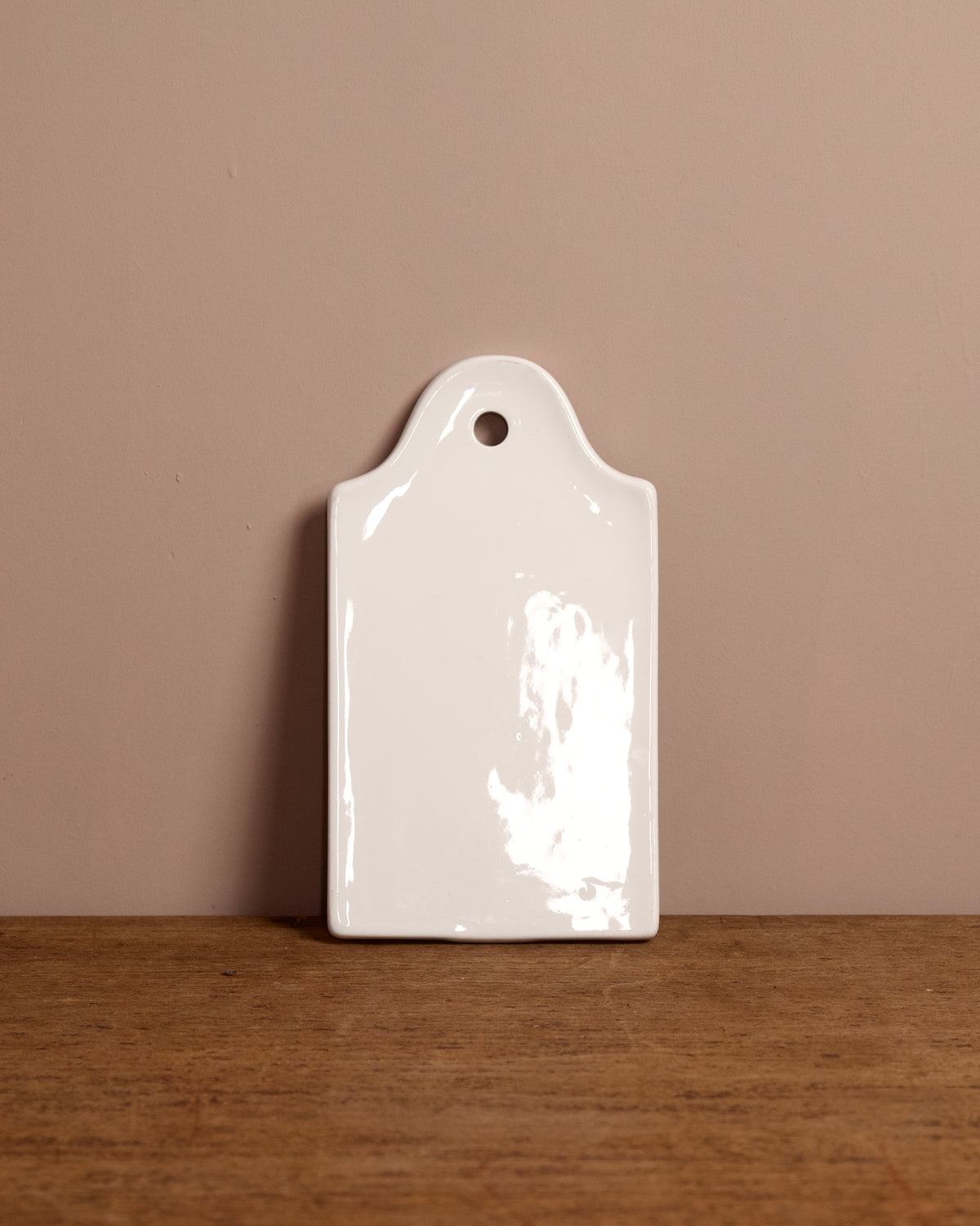 White ceramic cutting board with a hole on a wooden surface and beige wall background