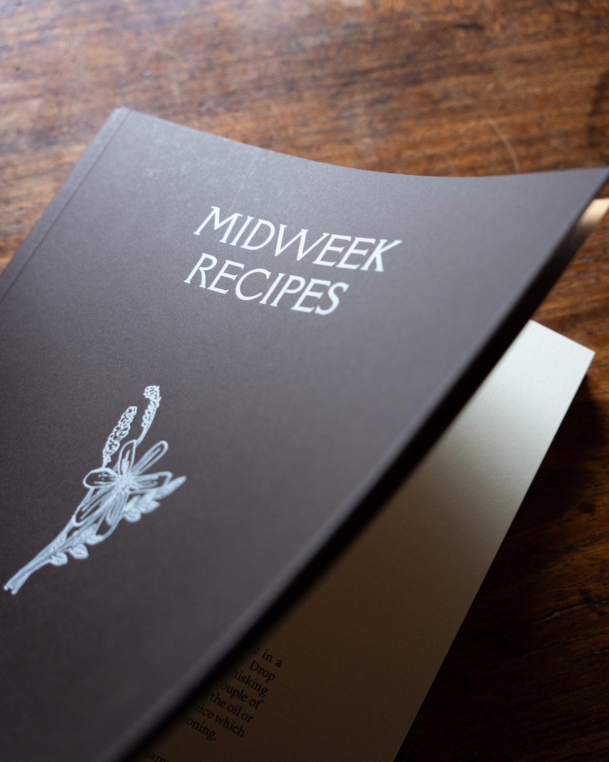 Cookbook titled 'Midweek Recipes' on a wooden surface