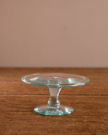 Clear glass cake stand on a wooden surface with a beige background