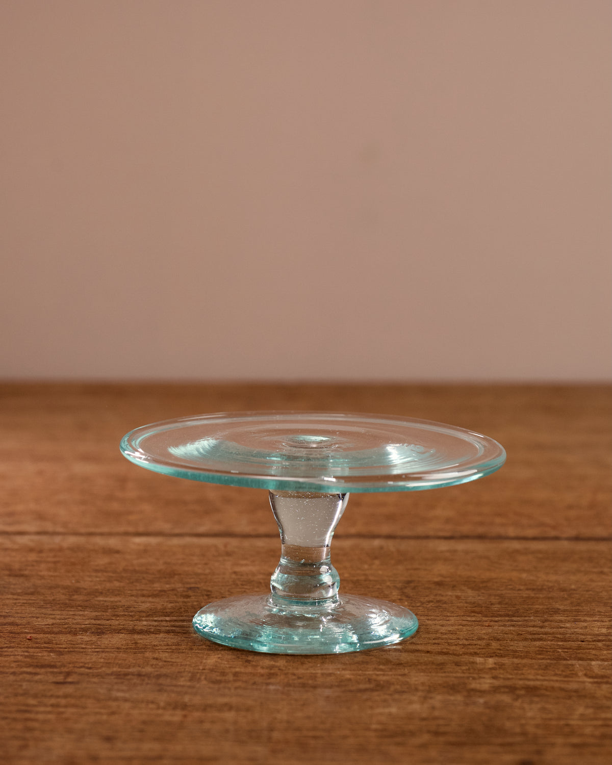 Clear glass cake stand on a wooden surface with a beige background