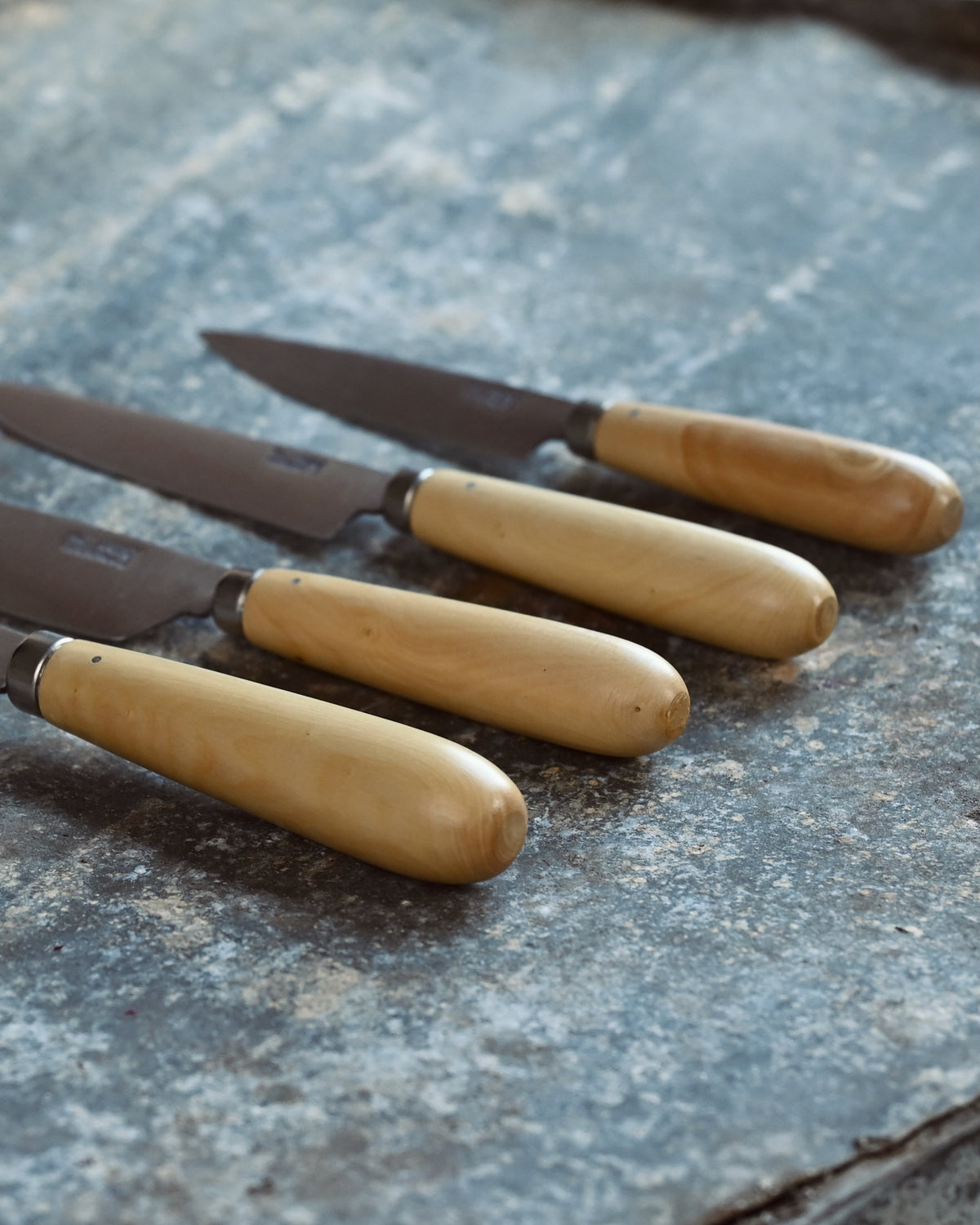 Set of four knives with wooden handles on a textured surface