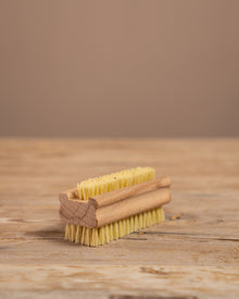 wooden nail brush with yellow bristles on a wooden surface and brown background