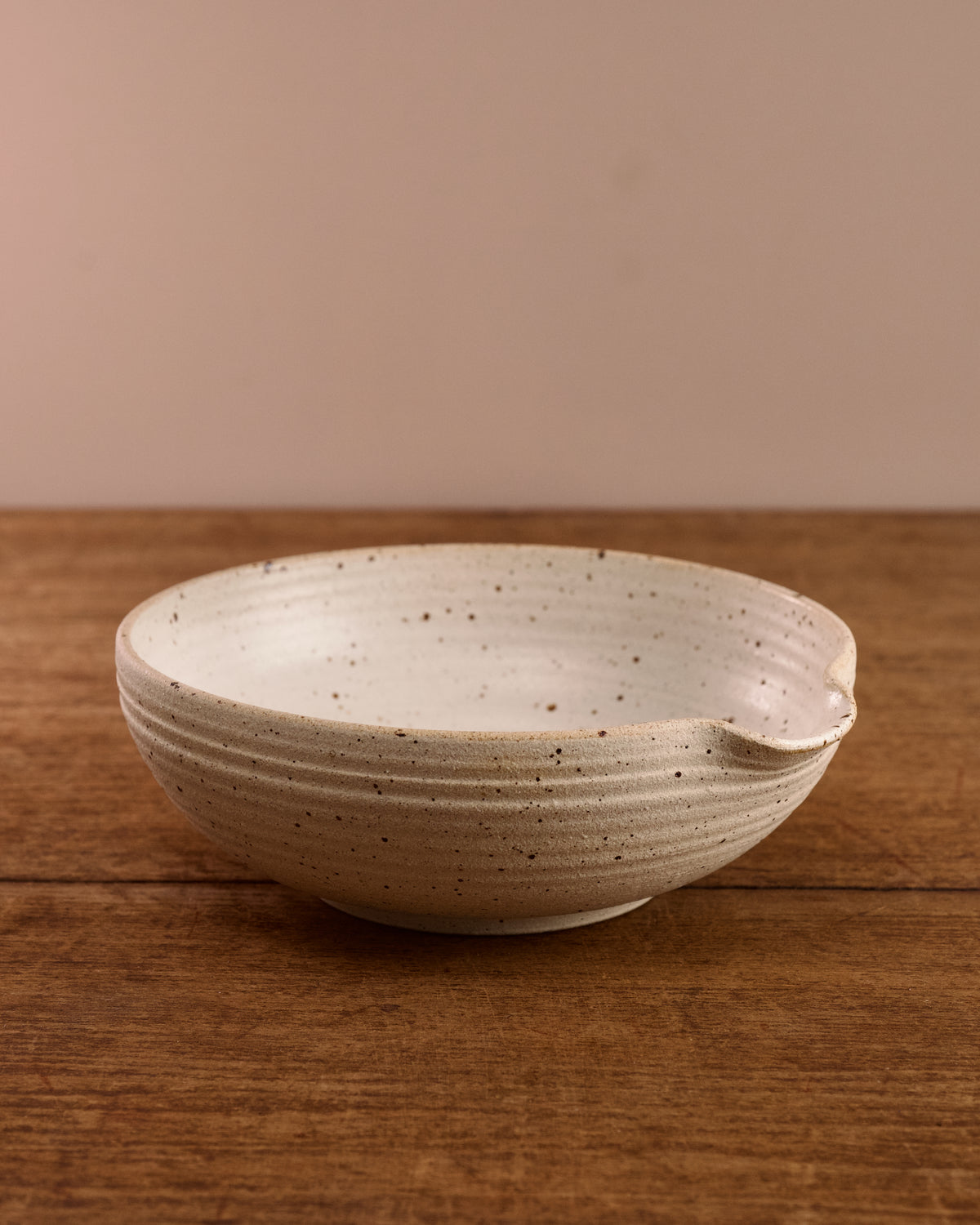Speckled ceramic mixing bowl on a wooden surface with a beige background