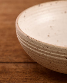 Speckled ceramic mixing bowl on a wooden surface with a beige background
