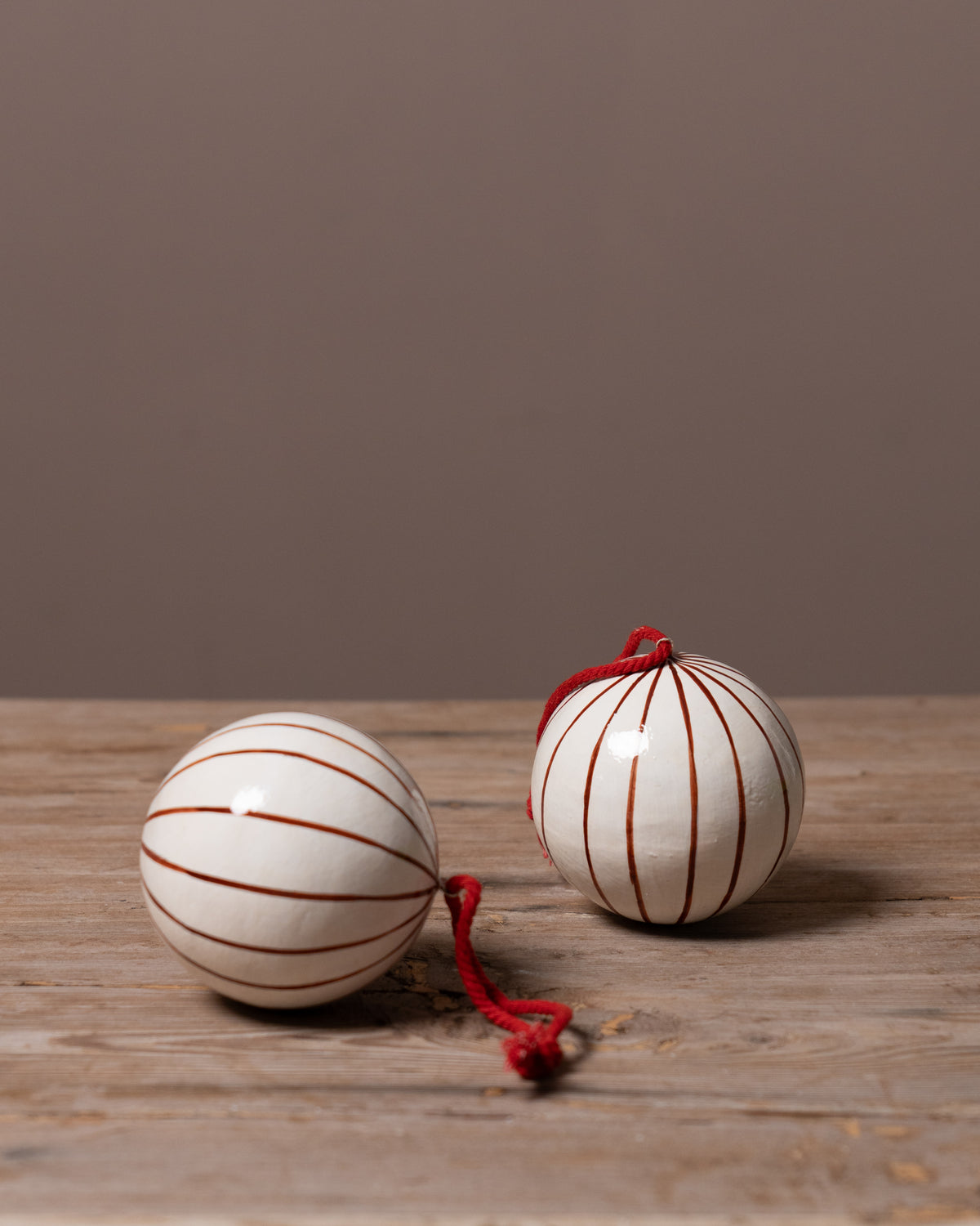 Two striped baubles with red string on a wooden surface against a brown background