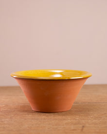 Ceramic bowl with yellow glazed interior and terracotta exterior on a wooden surface.