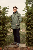 Person wearing a green Cook & Butler smock standing between two rows of plants.