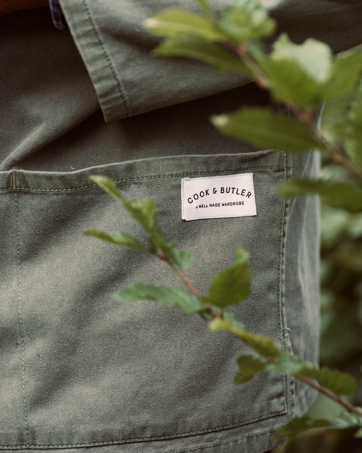 Green jacket with a 'Cook & Butler' label surrounded by greenery