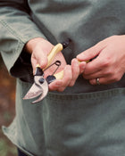 Person holding a pair of garden shears, wearing a green smock.