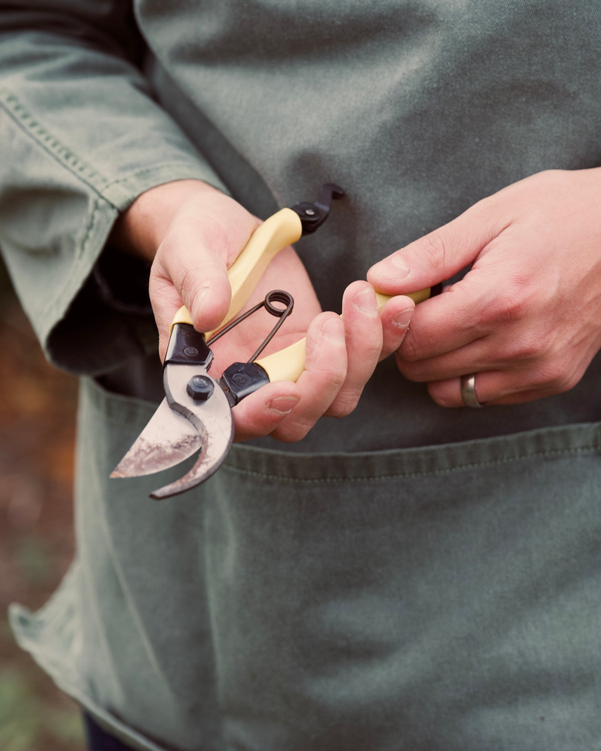 Person holding a pair of garden shears, wearing a green smock.