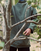 Person in a green smock holding an apple amidst tree branches