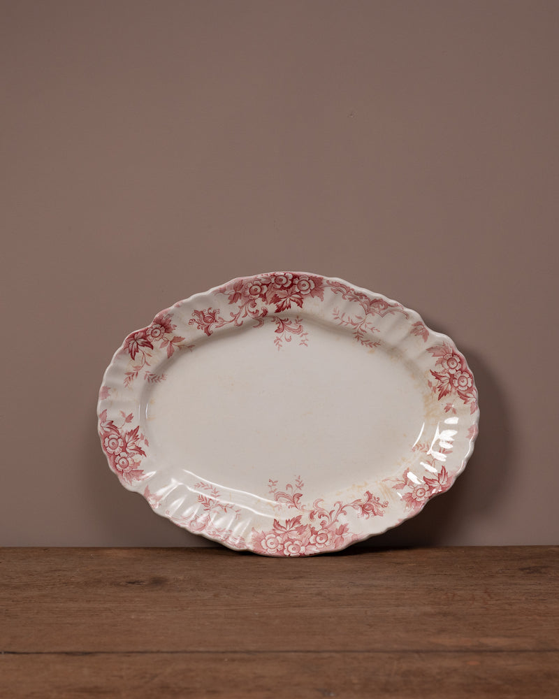 Decorative oval plate with red floral pattern on a wooden surface and brown background