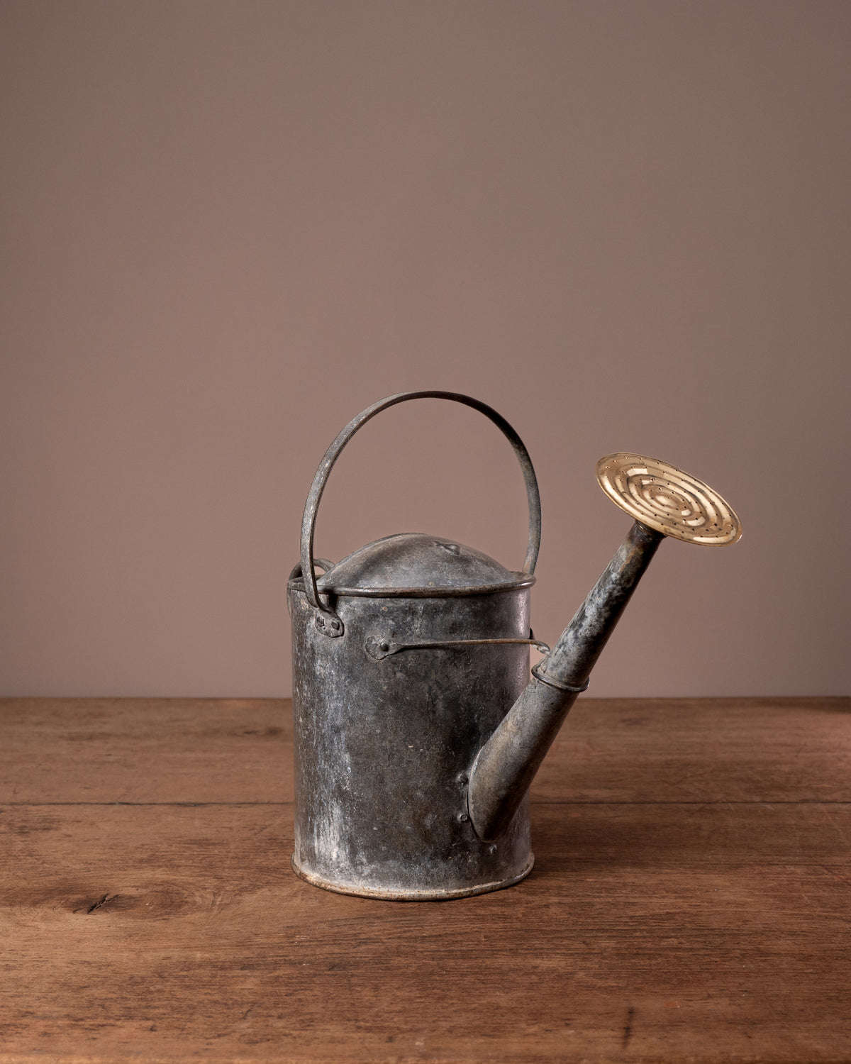 Vintage metal watering can on a wooden surface with a brown background