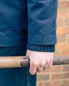 Person wearing a blue jacket holding a garden fork against a brick wall.