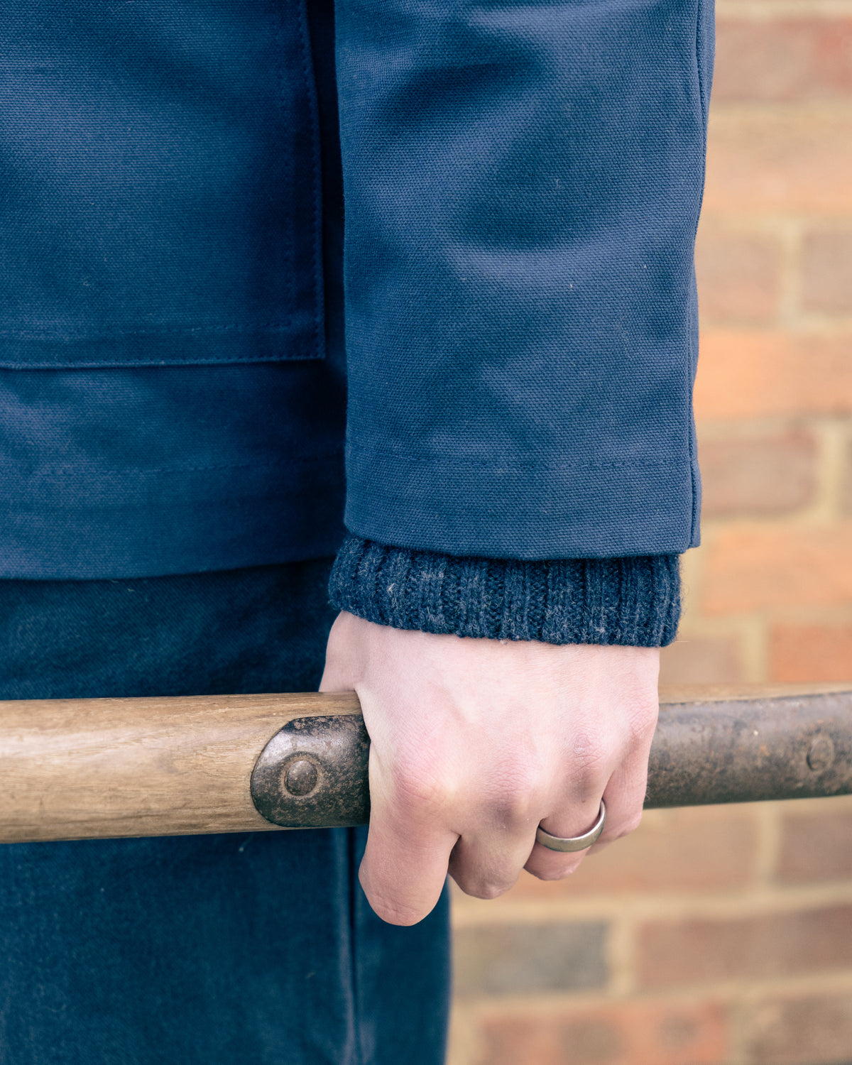 Person wearing a blue jacket holding a garden fork against a brick wall.