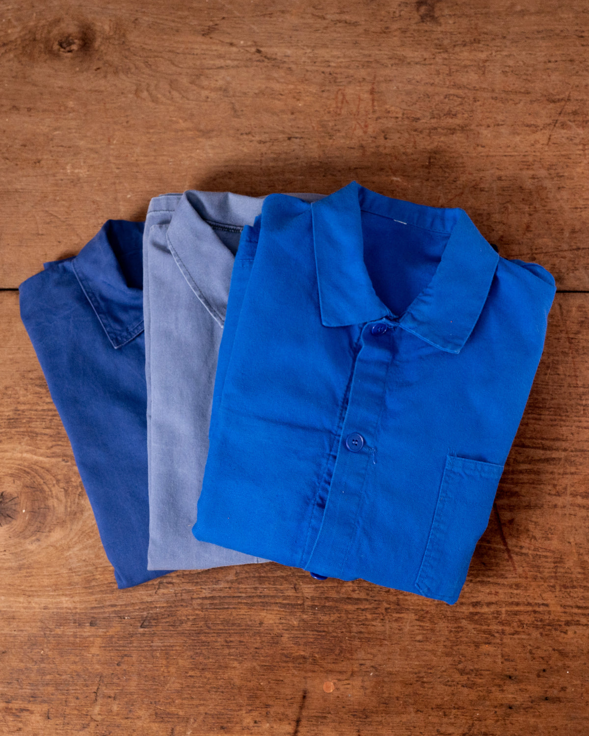 Folded blue work jackets on a wooden surface